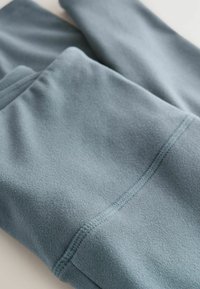 Un tissu en polaire bleu doux, avec une texture lisse et un léger éclat. Le design comprend des coutures nettes et un bord légèrement replié.