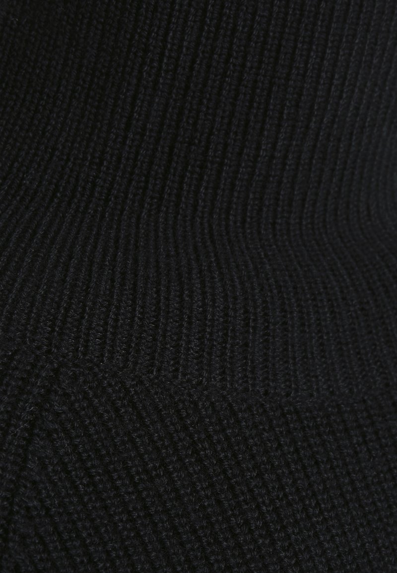 Gros plan sur un tissu en maille côtelée noire montrant des motifs de points verticaux et horizontaux détaillés avec de subtiles variations de texture.