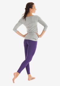 Grå langærmet top med bred udskæring, parret med tætsiddende lilla leggings. Toppen har et logo ved kanten og en glat tekstur.