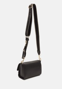 Bolso de hombro de piel negra con forma estructurada, herrajes dorados y una correa ancha que presenta el nombre de la marca y un ribete en contraste.