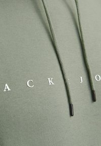 Olivengrøn hoodie med hvidt trykt tekst, med snoretræk med metalspidser og et blødt, tekstureret stof.
