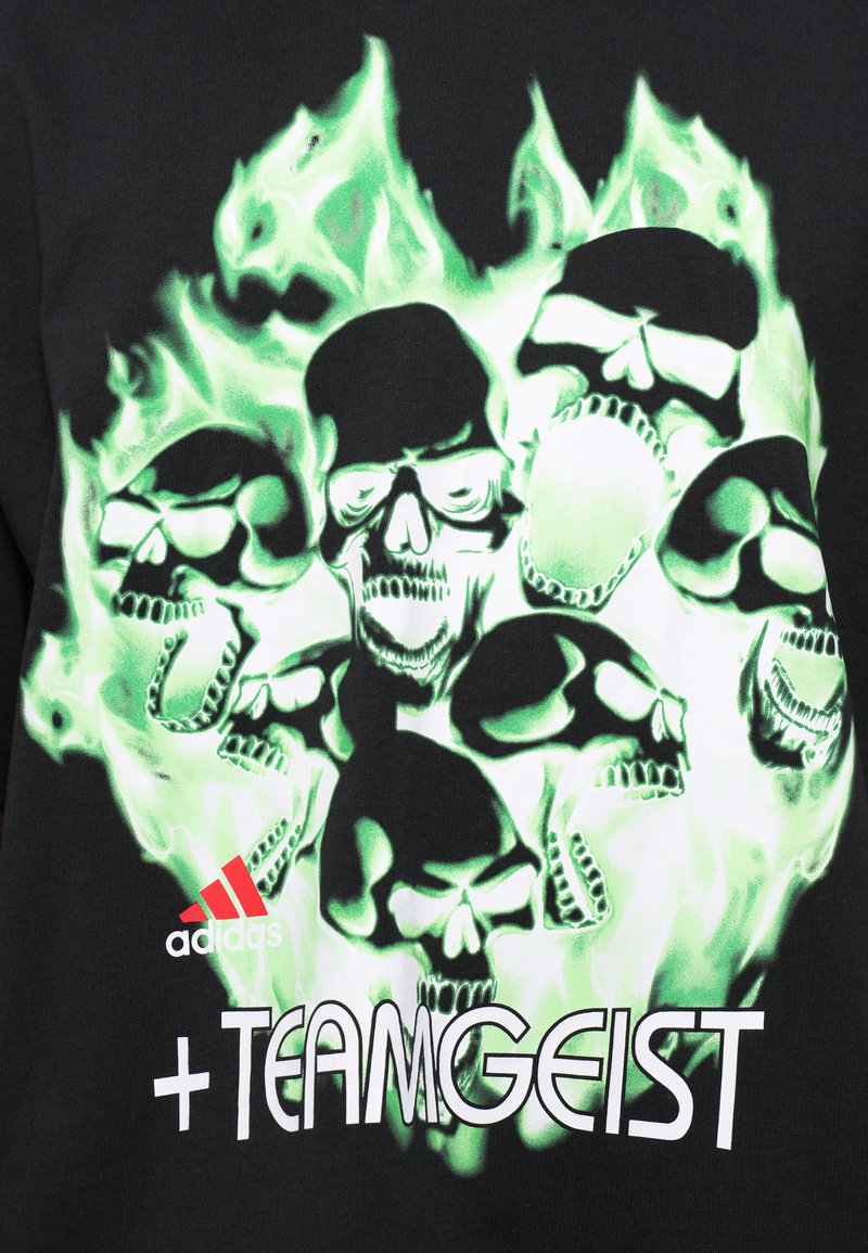 Camiseta negra con un gráfico central de llamas verdes y varios cráneos, con el logo "adidas" y el texto "+TEAMGEIST" en blanco.