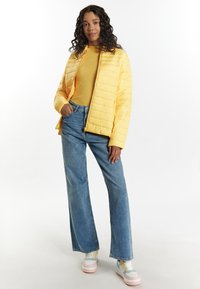 Gul puffjacka med horisontell sömnad, i kombination med en ribbad senapsgul tröja, ljusblå vida jeans och pastellfärgade sneakers.
