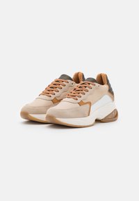 Scarpe sportive beige con accenti color cammello, materiali in suede e pelle, punta rotonda, colletto imbottito e suola in gomma spessa con una sezione trasparente.