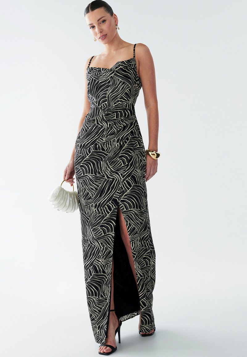 Vestido maxi en negro y crema con patrón de olas, cuenta con tirantes finos, una cintura ajustada y una abertura alta en el muslo. Los accesorios incluyen un bolso.