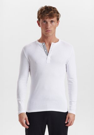 Hvid langærmet henley skjorte, som har knapper ved forkanten, en rund halsudskæring og et tekstureret sort stribedesign langs forkanten.