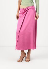 Pink stretch fabric maxi skirt with a twisted knot detail at the waist, featuring a smooth texture and a flowing silhouette.