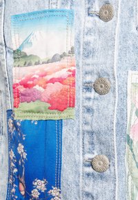 Denim jacket featuring three fabric patches: a blue floral pattern, a pink and green floral landscape, and a mountain scene with a blue sky.
