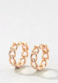 Boucles d'oreilles en forme de créoles de couleur dorée présentant un design de chaîne épaisse avec une texture lisse et des bords arrondis. Notables pour leurs maillons entrelacés.