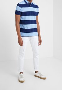 Camisa polo de rayas azul claro y marino, de manga corta y con cuello. Combinada con jeans blancos y zapatillas de colores claros.