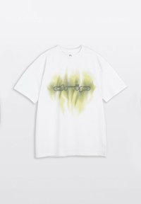 Biała, oversize t-shirt z zielono-żółtym wzorem płomieni i napisem "drip" w stylizowanej czarnej czcionce, umieszczony na środku przodu.