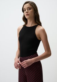 Zwarte mouwloze top met een geribbelde structuur, gecombineerd met hoog watertaille patronenbroek met een rood en blauw geometrisch ontwerp.
