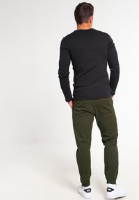 Zwart shirt met lange mouwen gecombineerd met olijfgroene broek, voorzien van een ontspannen pasvorm en elastische manchetten, afgewerkt met witte sneakers.