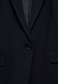 Blazer blu navy in tessuto morbido, con revers a punta, chiusura con un bottone nero singolo e due tasche laterali. Design minimalista con dettagli di cucitura discreti.
