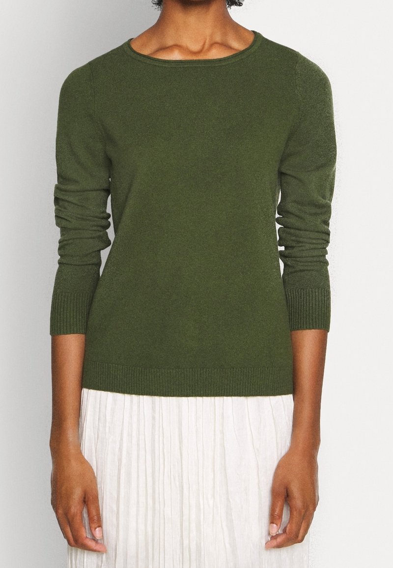 Olivgrön stickad tröja med rund hals och ribbade ärmar, buren över en vit plisserad kjol, har en mjuk textur och en figursydd design.