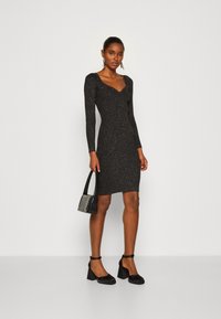 Black long-sleeve dress with a fitted silhouette, textured fabric featuring metallic threads, paired with black shoes and a small handbag.