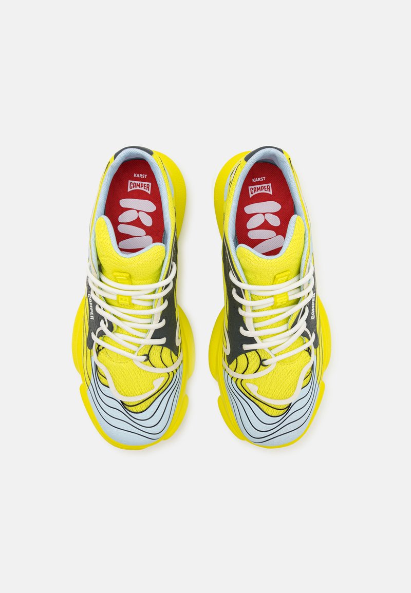 Żółte siatkowe sneakersy z niebieskimi i czarnymi akcentami, teksturowana podeszwa i białe sznurówki. Posiadają czerwoną wkładkę z logo.