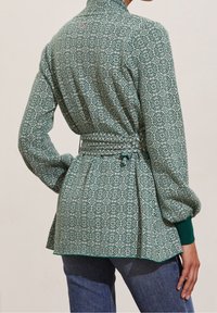 Vihreä kuvioitu paita, jossa on korkea kaulus, kapea vyötärö ja löysät hihnat. Sisältää kerättyä takaosaa ja kontrastiväriset hihansuut.