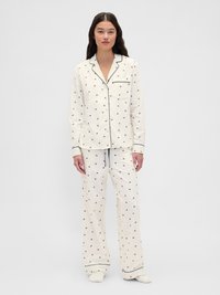 Ensemble de pyjama en coton crème avec accents bleu marine. Comprend un haut boutonné et un pantalon large à jambes droites, orné de petits motifs imprimés.