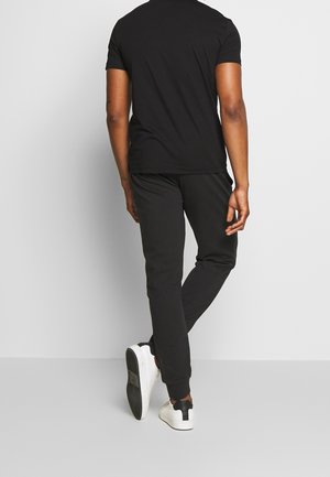 Czarny t-shirt z krótkim rękawem, zestawiony z czarnymi dresami i białymi trampkami. T-shirt ma okrągły dekolt, a spodnie wyposażone są w elastyczne mankiety.