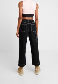 Pantalones de pierna ancha negros con costuras blancas en contraste, con bolsillos traseros y cintura alta, combinados con una camiseta corta rosa.
