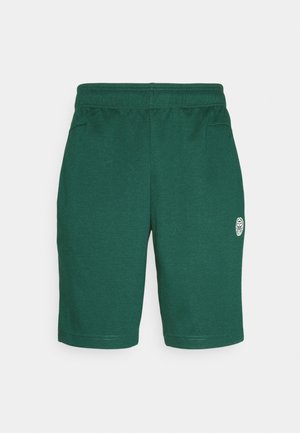Grüne knielange Shorts mit elastischem Bund und kleinem weißem Kreislogo am linken Oberschenkel, vor schlichtem hellem Hintergrund gezeigt.