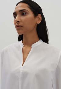 White cotton shirt with a stand-up collar, featuring a partial button placket and a smooth texture, displayed on a neutral background.