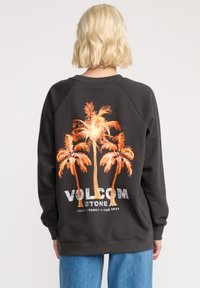 Donkergrijze sweatshirt met oranje palmboomgrafiek en "VOLCOM"-tekst op de achterkant. Heeft raglanmouwen en ribbenboorden.