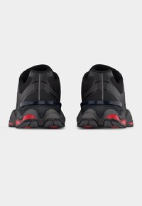 Ζευγάρι μαύρα αθλητικά παπούτσια με χοντρές σόλες, κόκκινες λεπτομέρειες στις φτέρνες και τις μύτες, από πίσω, με φόντο ένα απλό ανοιχτόχρωμο φόντο.