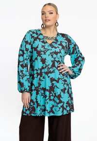 Tunique florale anthracite avec des motifs turquoise, dotée d'un col en V et de manches longues. Associée à un pantalon marron ample, en tissu lisse.