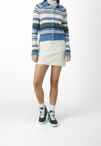 Randig stickad cardigan i blått, grönt, rosa och vitt; matchad med en krämfärgad denimkjol och gröna högskurna sneakers. Vita ankelsockor.