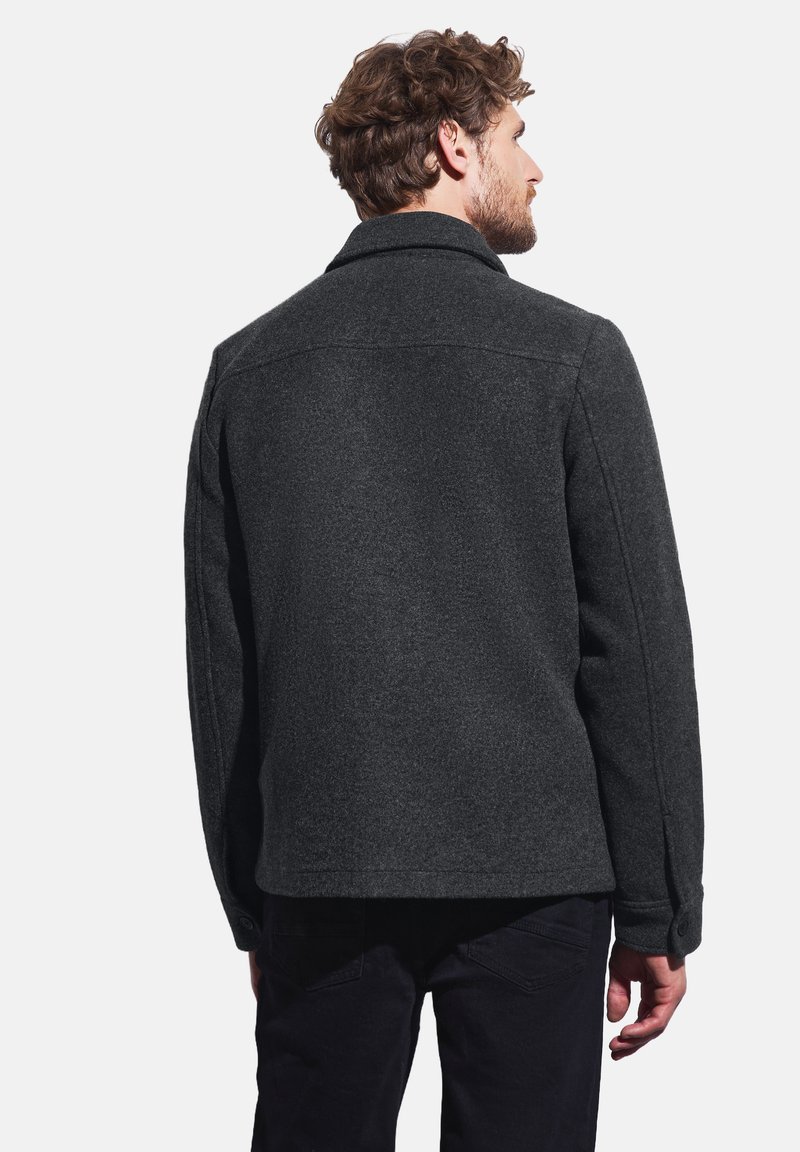 Mörkgrå ulljacka med rak skärning, spetsig krage och knäppning vid ärmsluten. Har en texturerad yta och en enkel, avskild stil.