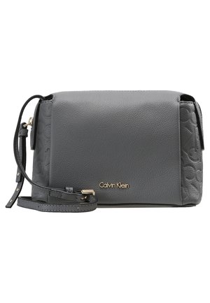 Sac bandoulière Calvin Klein en cuir grainé gris avec sangle ajustable et logo embossé subtil sur le côté.
