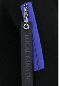 Zwarte stof met een paarse rits, waarvan een zwart label met de tekst "LOCAL FANATIC" in grijze letters aan de ritshendel is bevestigd.