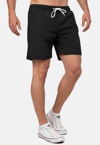 Pantaloni da nuoto neri con cintura elastica e lacci bianchi, caratterizzati da una trama liscia e un piccolo dettaglio del logo sull'orlo.