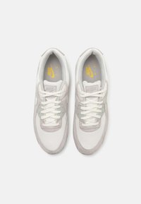 Nike sneakers with a white mesh upper, gray suede accents, and white laces. Features Nike branding in yellow on the insole.