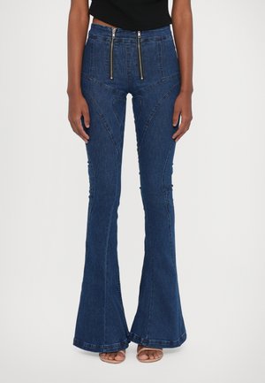Flared denim jeans in deep blue, featuring two front zippers, a high waist, and diagonal stitching patterns for added detail and shape.