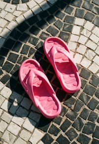 Paire de sandales Havaianas roses sur un sol en mosaïque noir et blanc avec la lumière du soleil et des ombres créant du contraste.