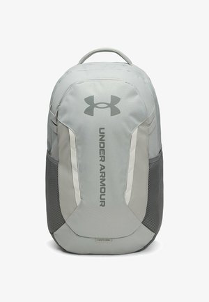 Lichtgrijze Under Armour rugzak met bovenhandvat, mesh zijvakken en verticale logotekst op het voorpaneel.