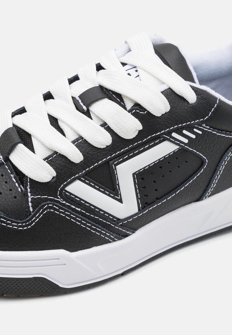 Baskets noires avec lacets blancs, présentant un dessus en cuir texturé, des accents blancs, des détails perforés et des coutures contrastées.