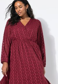 Bordeaux jurk met een wikkelontwerp, textiele stof met een geometrisch patroon en lange mouwen. Elastische taille zorgt voor een gedrapeerd effect.