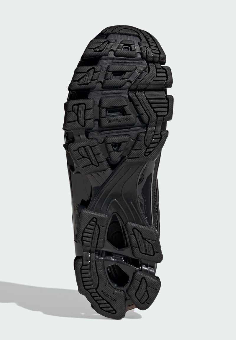 Semelle de chaussure de sport noire en caoutchouc texturé, équipée d'une bande de roulement à motifs pour une meilleure adhérence et de rainures distinctes assurant flexibilité et traction.