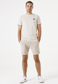 Camiseta de rayas beige claro con mangas cortas, que presenta un pequeño logo en el pecho; combinada con pantalones cortos de pana beige claro.