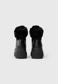Schwarze Knöchelstiefel mit strukturiertem Kunstfellkragen, Gummisohlen und gemusterten Details auf dem Lederoberteil. Chunky Plattformdesign.