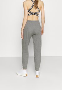 Grijze sweatpants met een taps toelopend ontwerp en elastische tailleband, gecombineerd met een zwart-wit sportbeha en witte sneakers.
