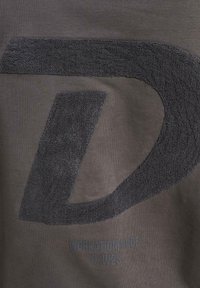 Sivi pamučni majica s teksturiranim crnim logotipom slova "D" i natpisom "WORKATION MODE F/W23" u tamnijoj sivoj boji na dnu.