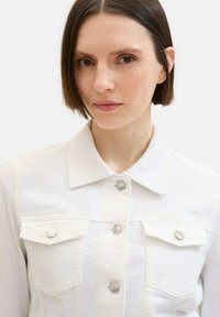 White denim jacket featuring a classic collar, silver snap buttons, and two chest pockets with flaps. Smooth texture and tailored fit.