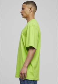 Neon grün, übergroßes T-Shirt aus Baumwolle. Kurze Ärmel, Rundhalsausschnitt, lockere Passform und glatte Textur. Getragen mit blauen Jeans.
