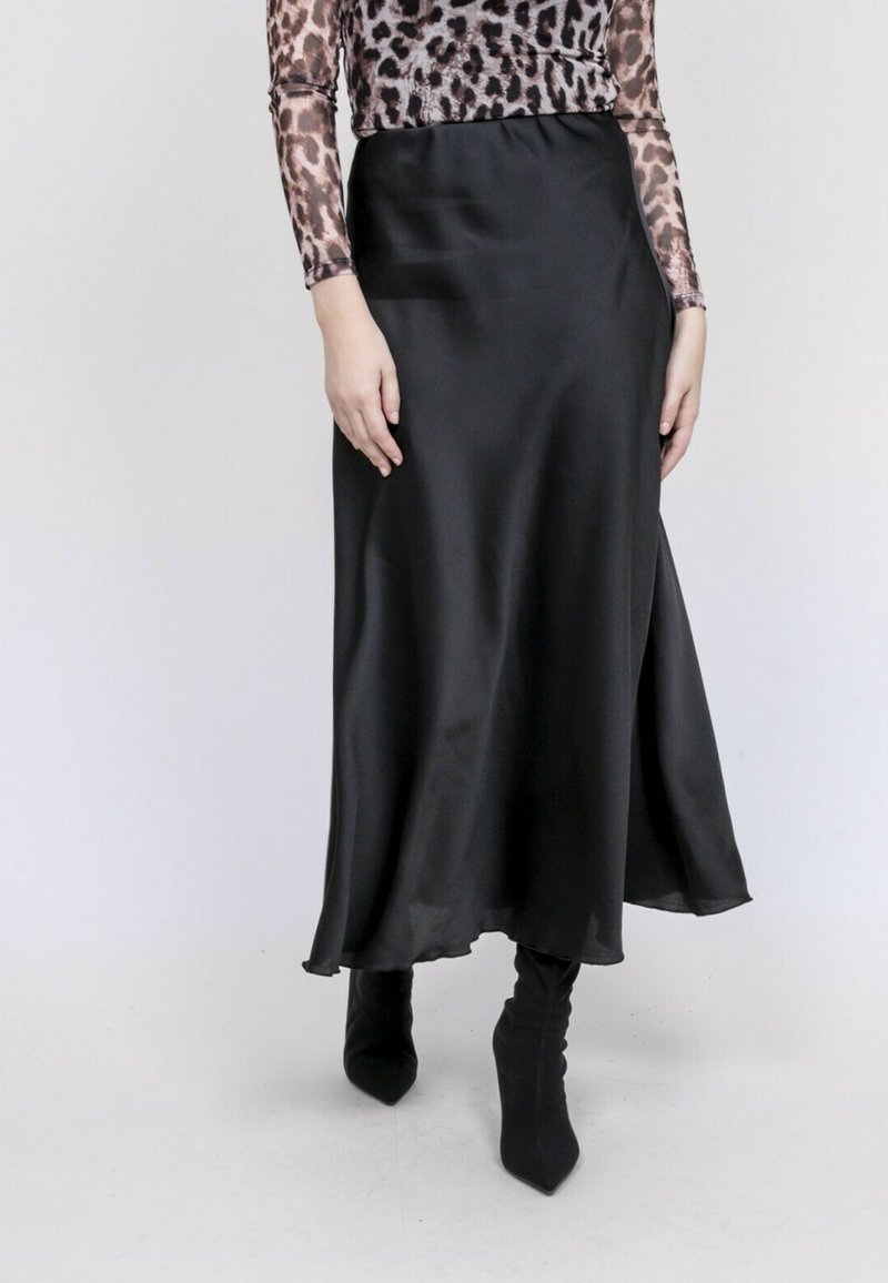 Jupe maxi en satin noir avec un design fluide. Elle présente une texture lisse et un léger éclat, complétée par des bottines noires moulantes.