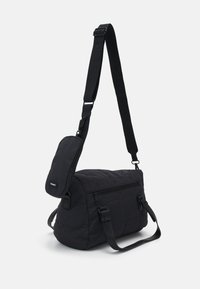 Schwarze gesteppte Schultertasche mit verstellbarem Tragegurt, Reißverschlusstaschen und einem kleinen abnehmbaren Etui. Hergestellt aus strapazierfähigem Stoff mit glatter Textur.